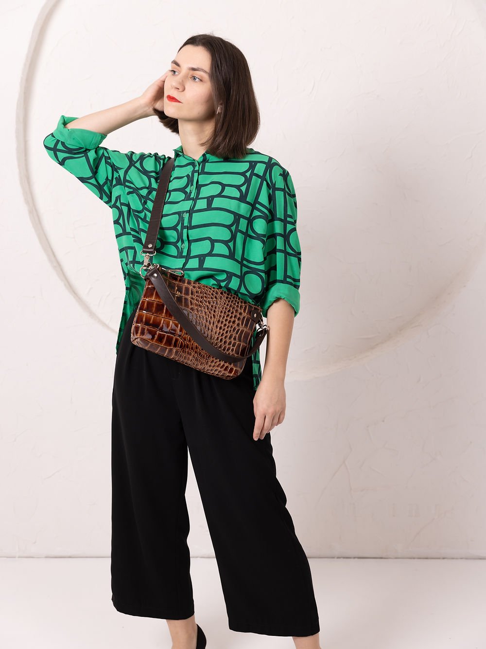 2. Woman wearing TOKS VISOKS TOMMY leather bag with alligator pattern, styled crossbody with green shirt