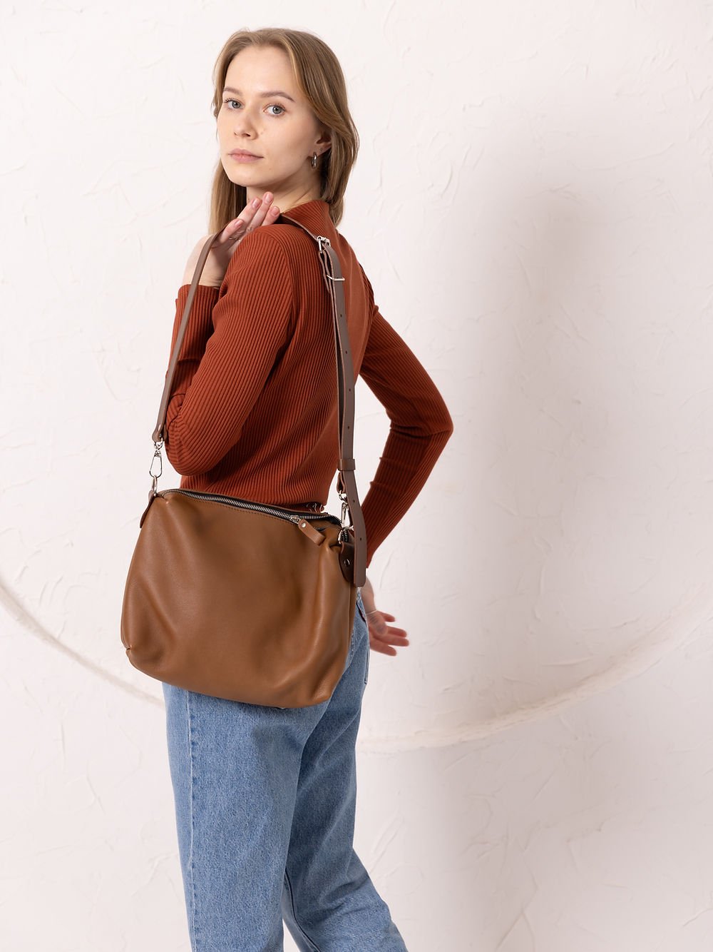 1. Woman wearing TOKS VISOKS ROBIN leather handbag in camel brown, shown in lifestyle setting