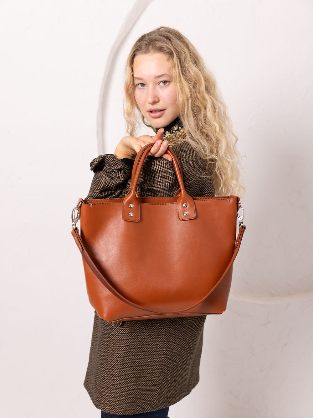 1. Woman holding TOKS VISOKS MIGLE leather handbag in ginger, showcasing style and practicality