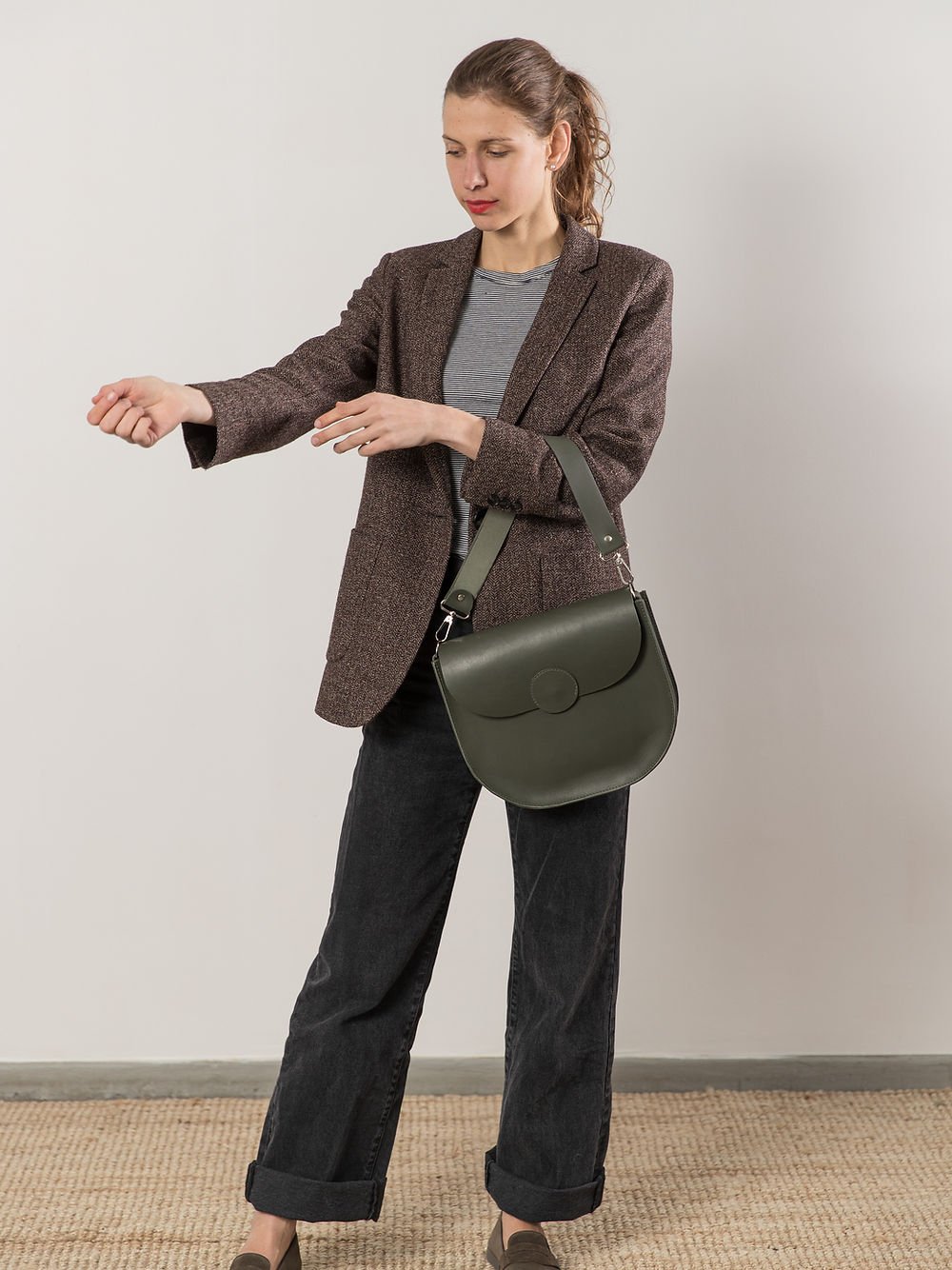 6. Woman adjusting sleeve while wearing TOKS VISOKS FIONA Handbag in faded green, studio shot