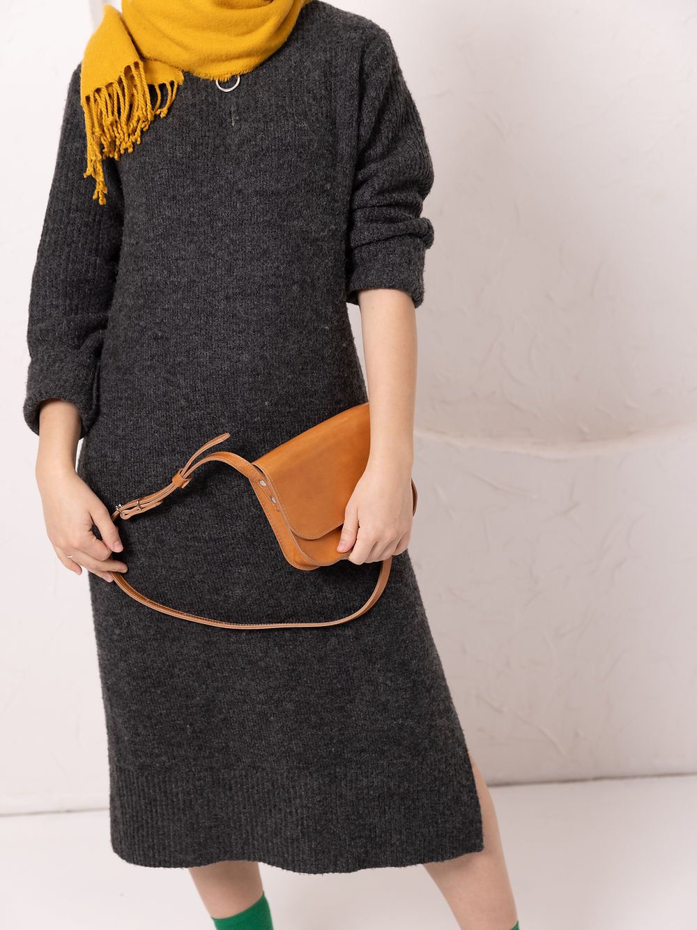 7. Woman holding TOKS VISOKS RUBY Purse in caramel leather, styled with yellow scarf and dark dress