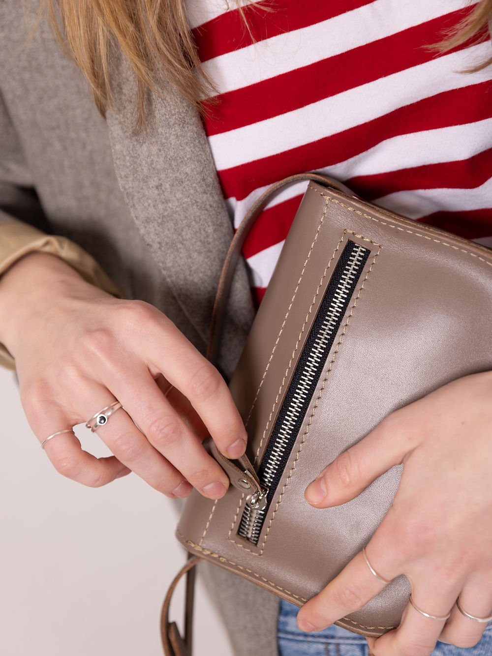 6. Close-up of woman opening zipper on TOKS VISOKS RUBY Purse in beige, highlighting recycled leather
