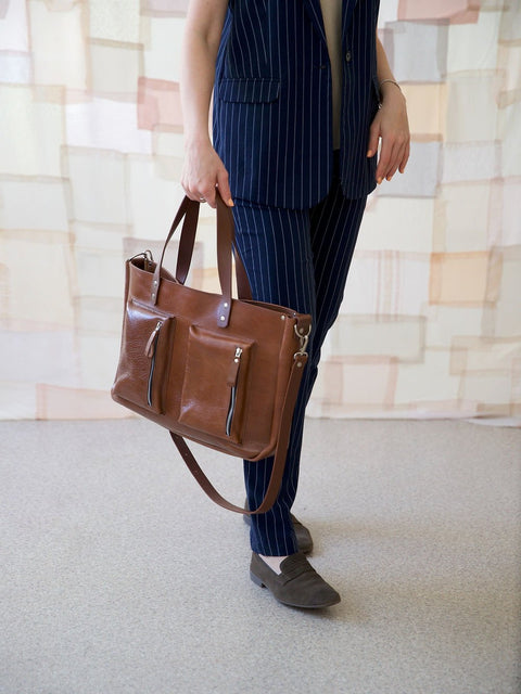 1. Woman holding TOKS VISOKS AMBER handbag in brown recycled leather, styled with pinstripe suit