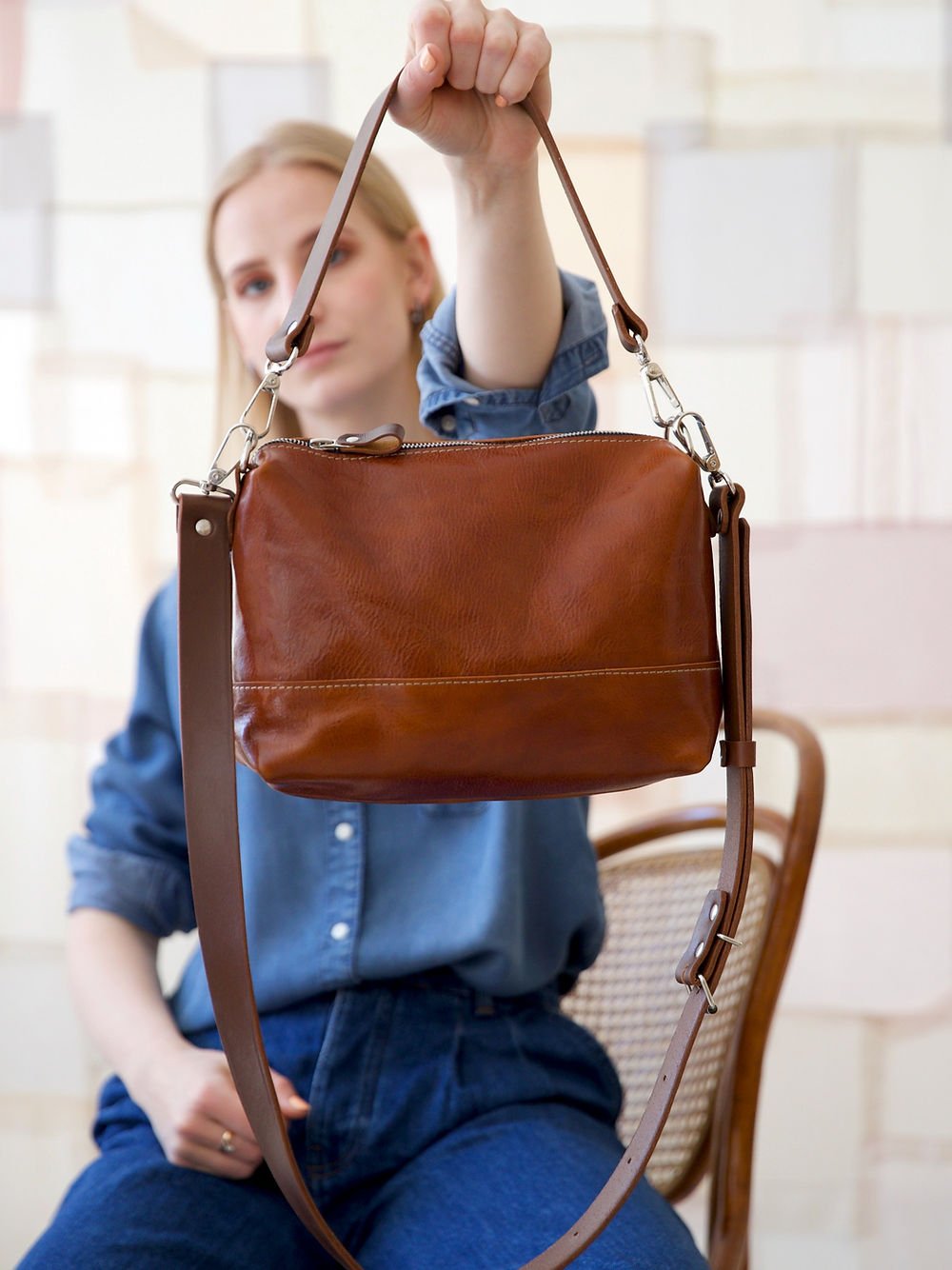 6. Woman displaying TOKS VISOKS ROBIN leather handbag in ginger brown, highlighting adjustable handles
