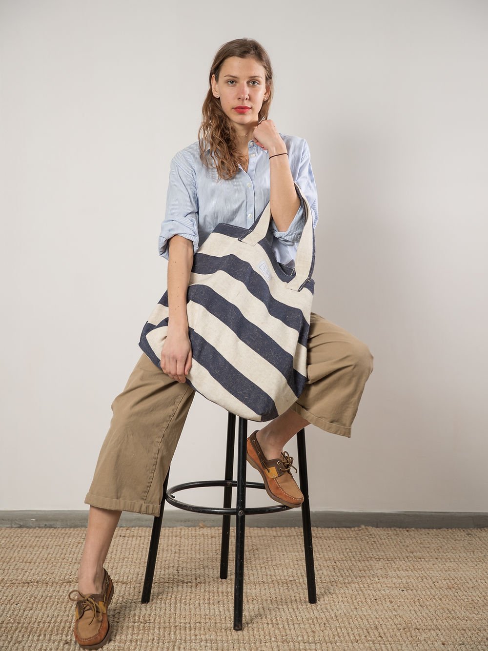 6. Woman sitting with TOKS VISOKS oversized beach bag in reclaimed stripe canvas, studio setting