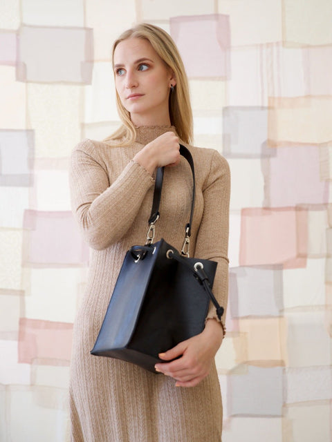 5. Woman holding black TOKS VISOKS PIPER Purse, showcasing vegetable-dyed leather finish, lifestyle setting