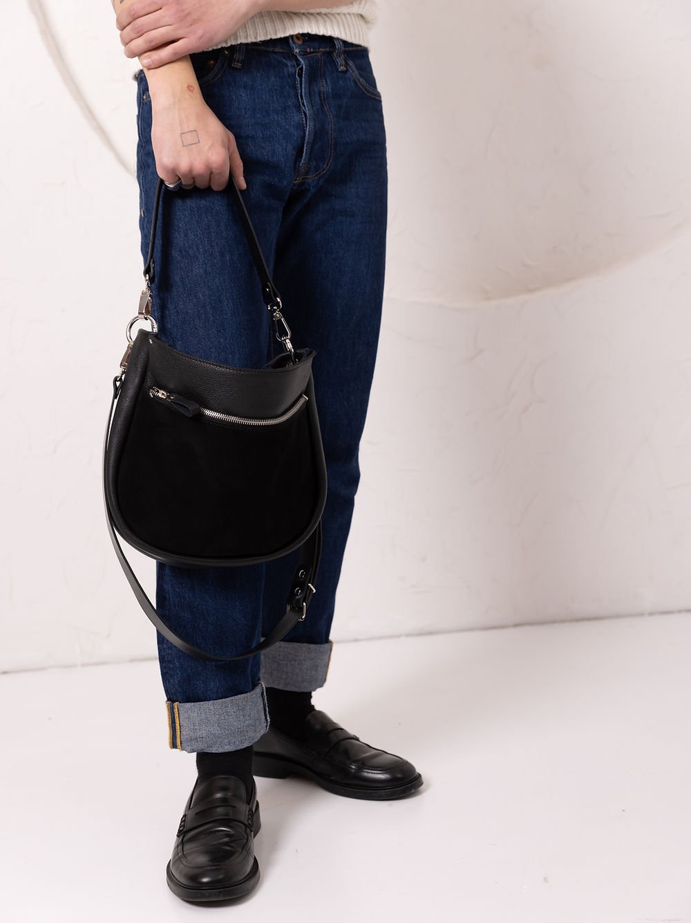 6. Unisex model displaying TOKS VISOKS STELLA black leather handbag with adjustable strap, styled with casual attire in studio