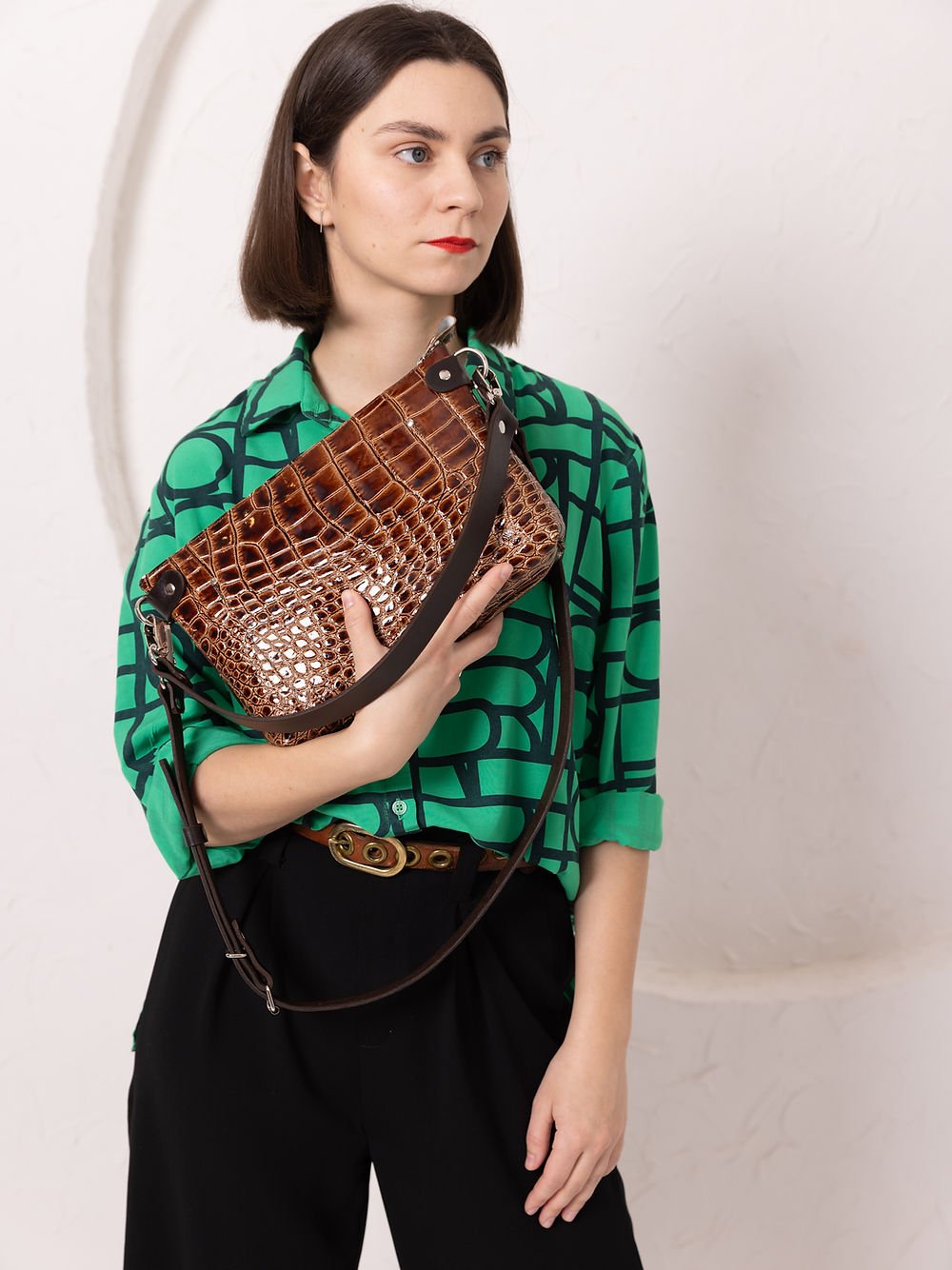 5. Woman holding TOKS VISOKS TOMMY leather bag with alligator pattern, shown in studio setting