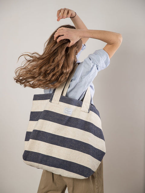 2. Woman holding TOKS VISOKS striped canvas beach bag, shown from the back in lifestyle setting