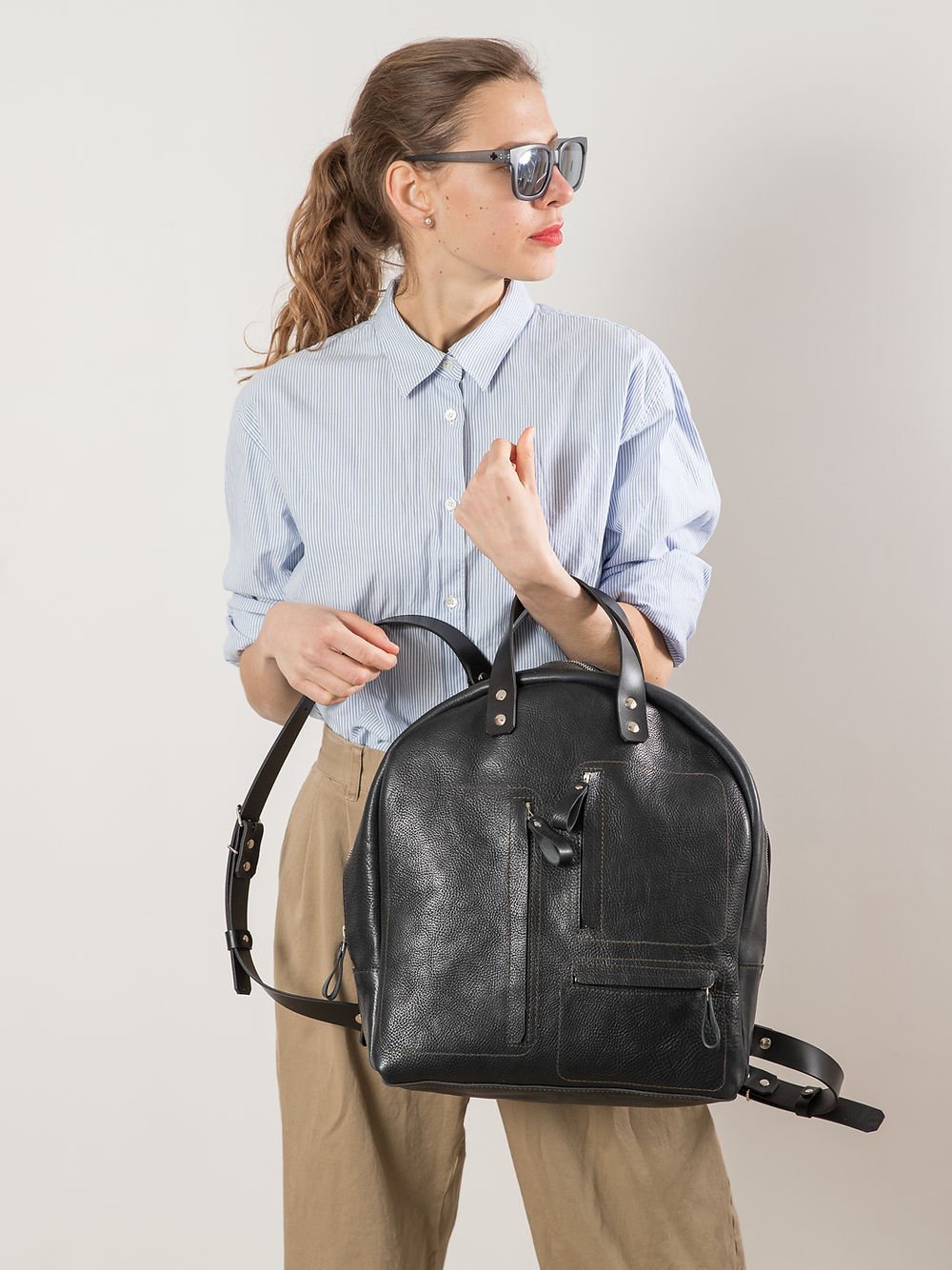 7. Woman holding TOKS VISOKS GORDON Backpack in dark denim, highlighting handmade leather texture