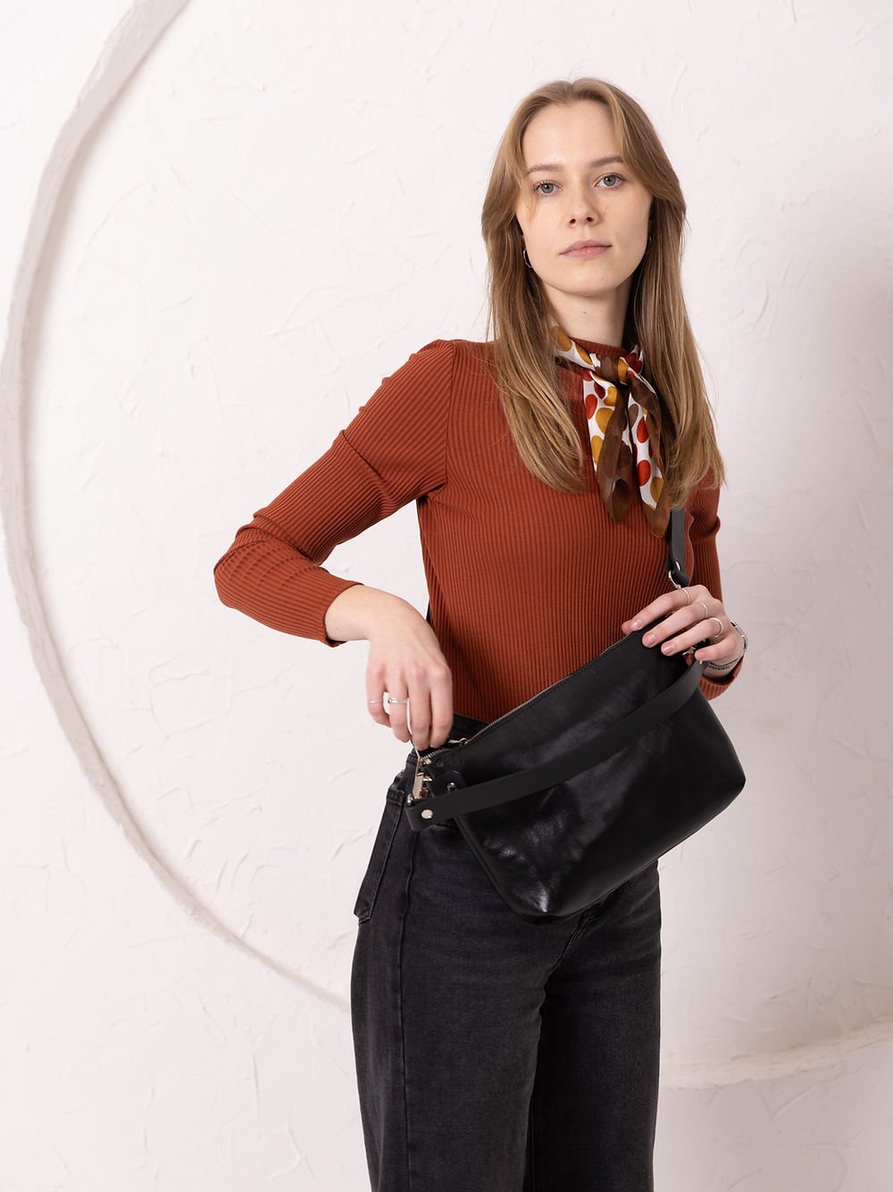 9. Women's black TOMMY leather bag by TOKS VISOKS worn crossbody, front view in studio setting