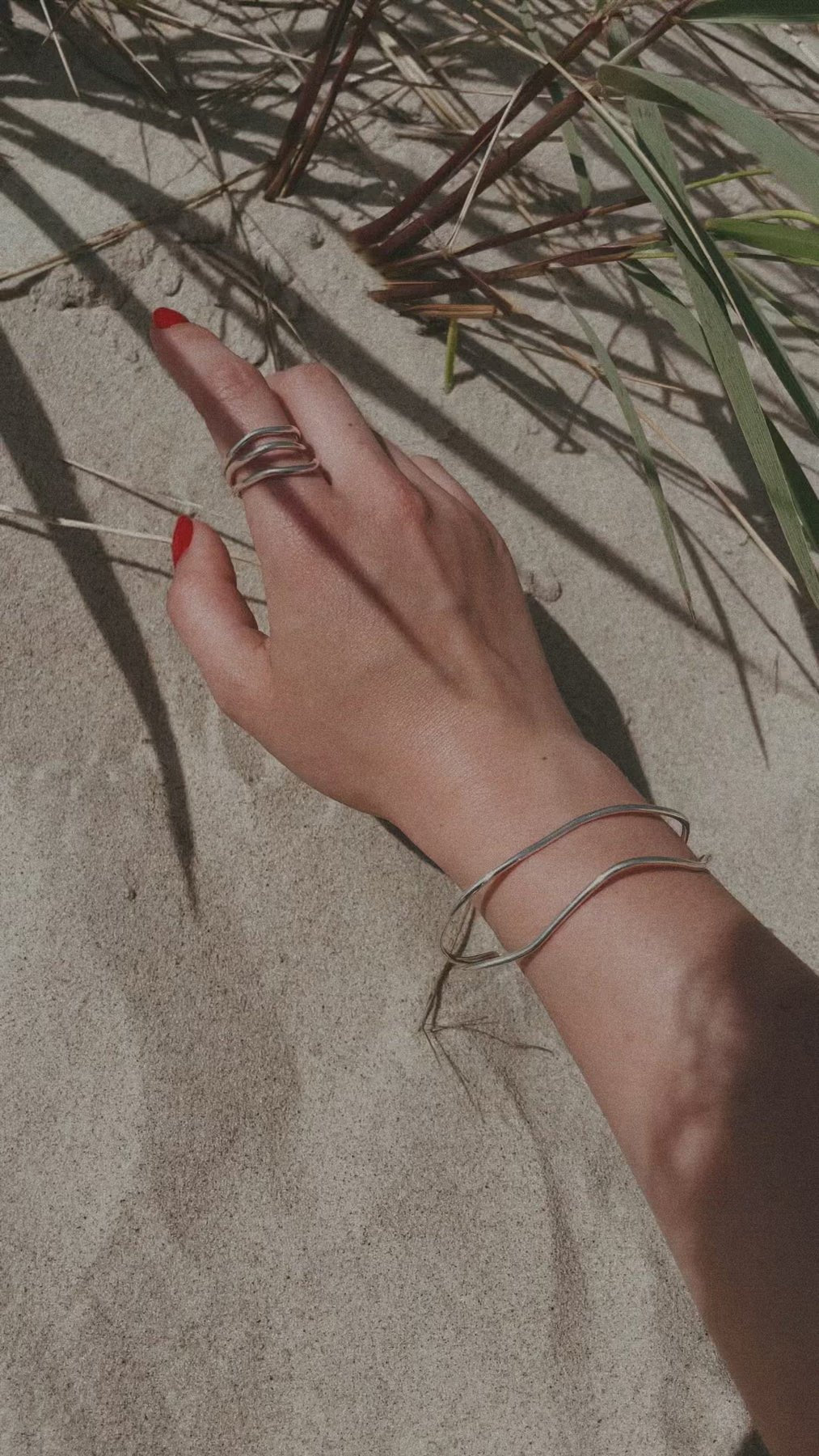 3. Woman's hand with NO MORE Reef Break Wave Ring in sterling silver, shown on sand with natural elements