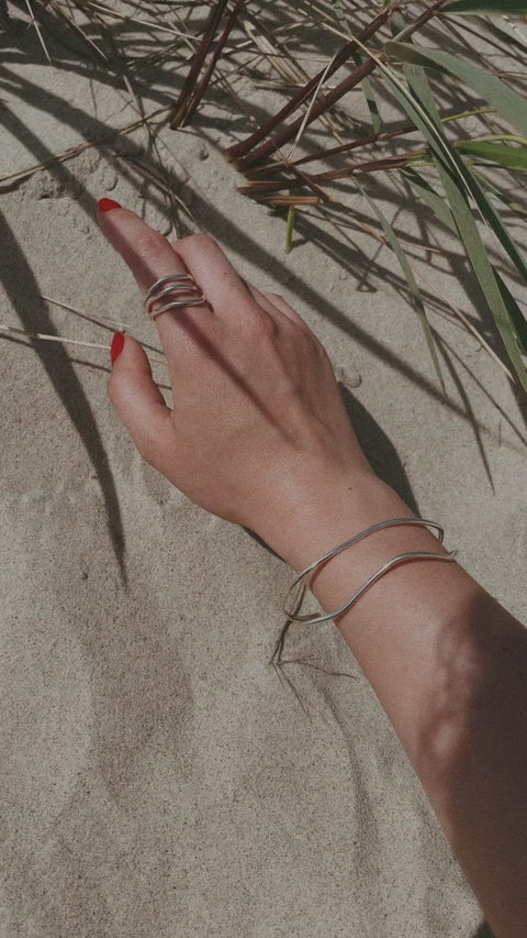 3. Woman's hand with NO MORE Reef Break Wave Ring in sterling silver, shown on sand with natural elements