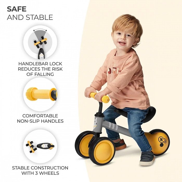 1. Child riding yellow Kinderkraft CUTIE balance bike with non-slip handles and stable construction indoors