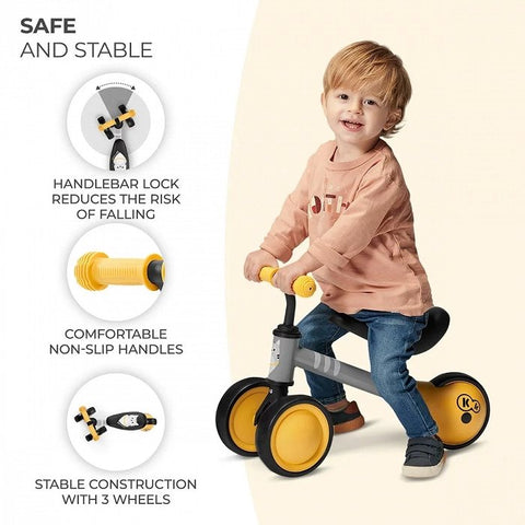 1. Child riding yellow Kinderkraft CUTIE balance bike with non-slip handles and stable construction indoors