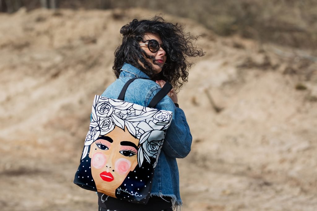 1. Woman wearing Garbanota HANDBAG YOKO in black with artistic print, outdoor setting