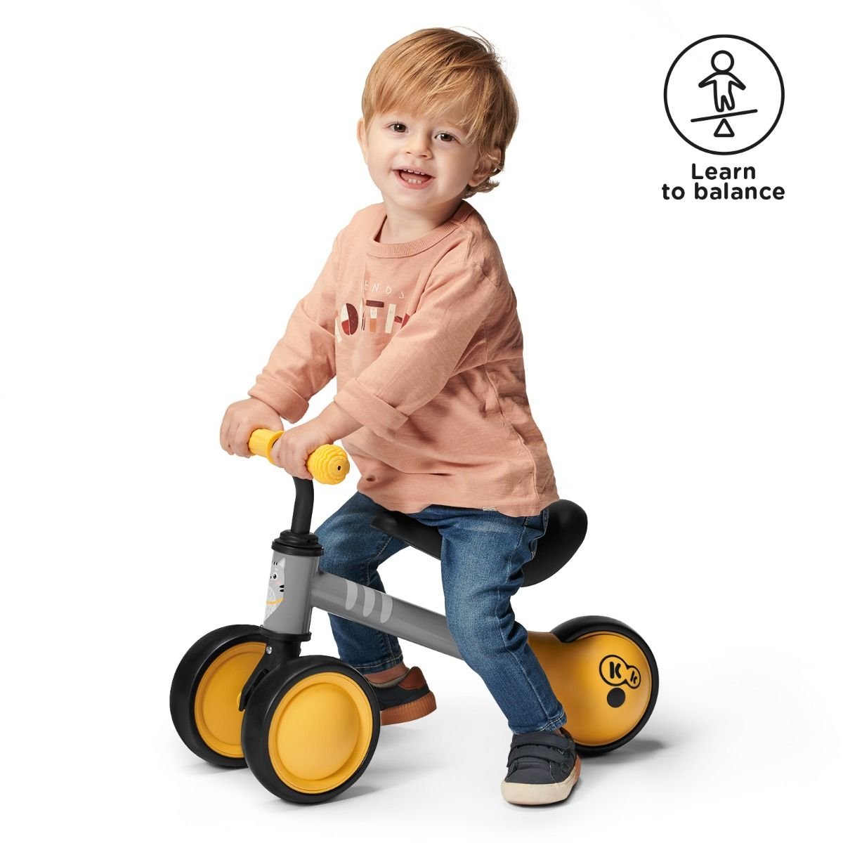 13. Child smiling while riding yellow Kinderkraft CUTIE balance bike indoors
