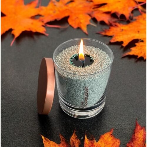 4. Candledust emerald powder candle in glass with open lid, lit among autumn leaves