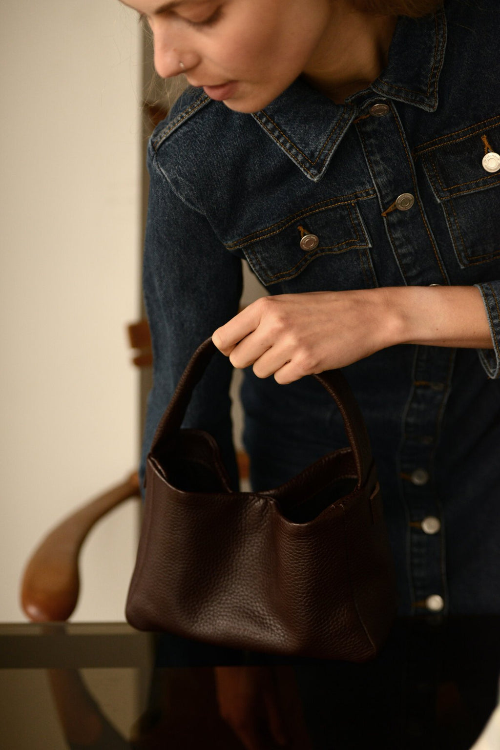 4. Woman in denim jacket holding Lava flow Crossbody Bag MERU in dark brown leather