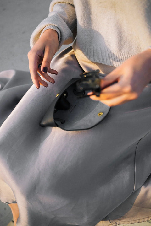 3. Woman opening Mirgoods black leather sunglasses case, highlighting soft lining, lifestyle setting