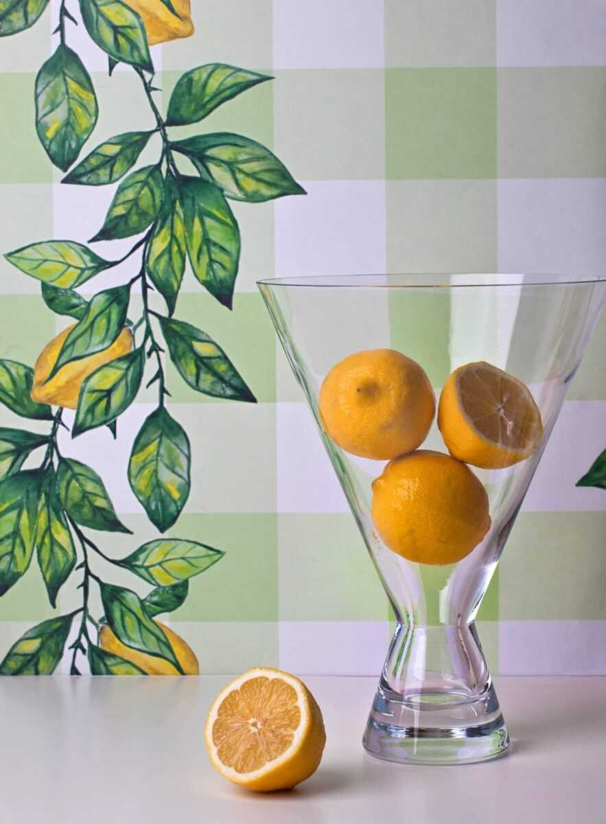 2. Glass vase with lemons in front of Lemon Branch wallpaper featuring green leaves and yellow lemons