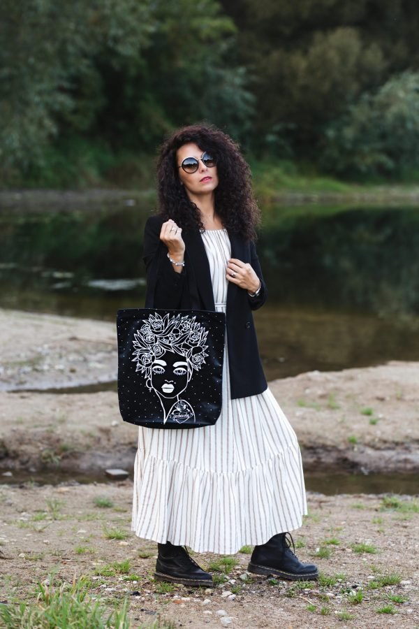 4. Woman posing with Garbanota Naomi handbag in black, floral haircut design, styled with a long dress by a lake
