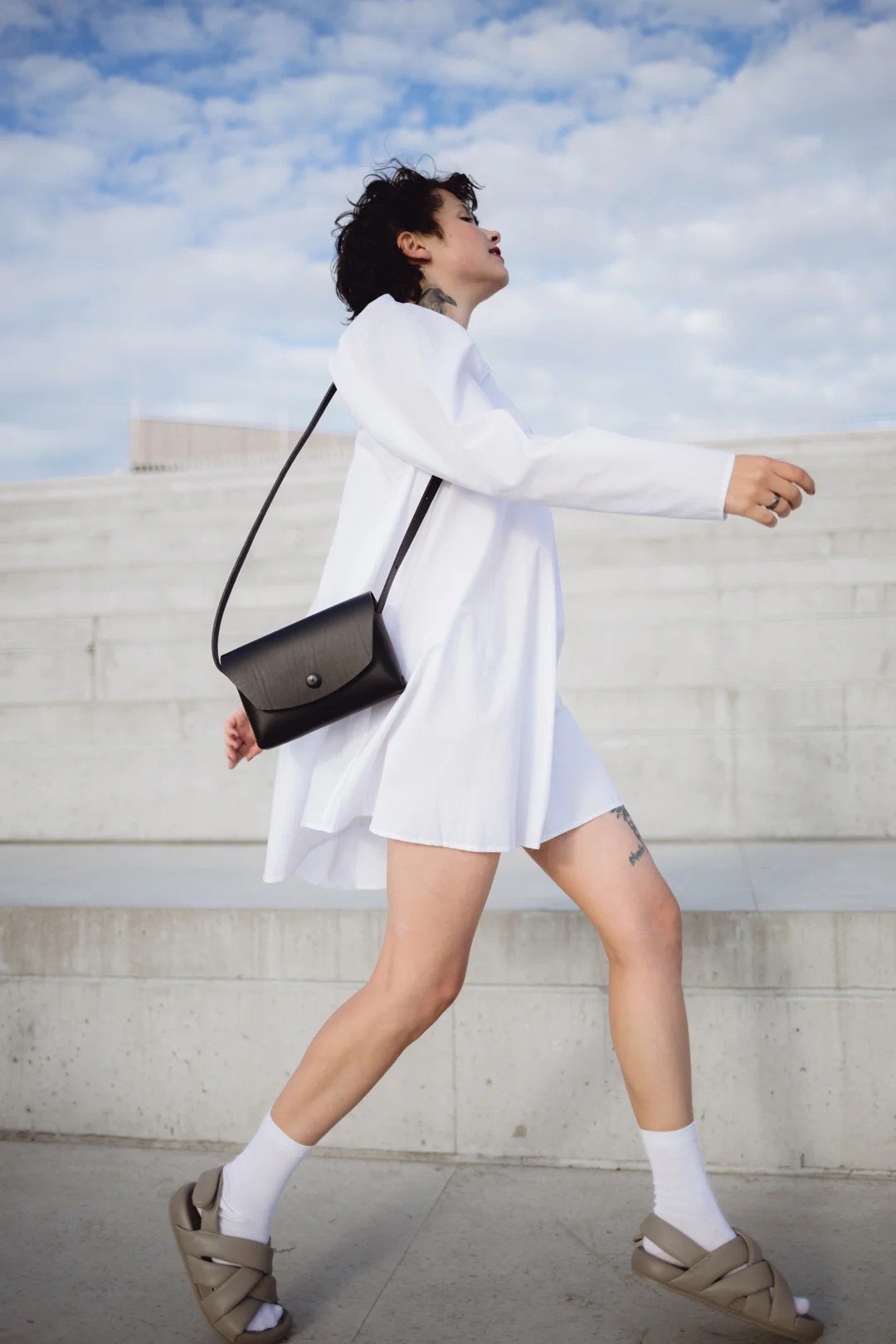 1. Woman walking outdoors wearing a white dress and carrying a Mirgoods black leather clutch bag