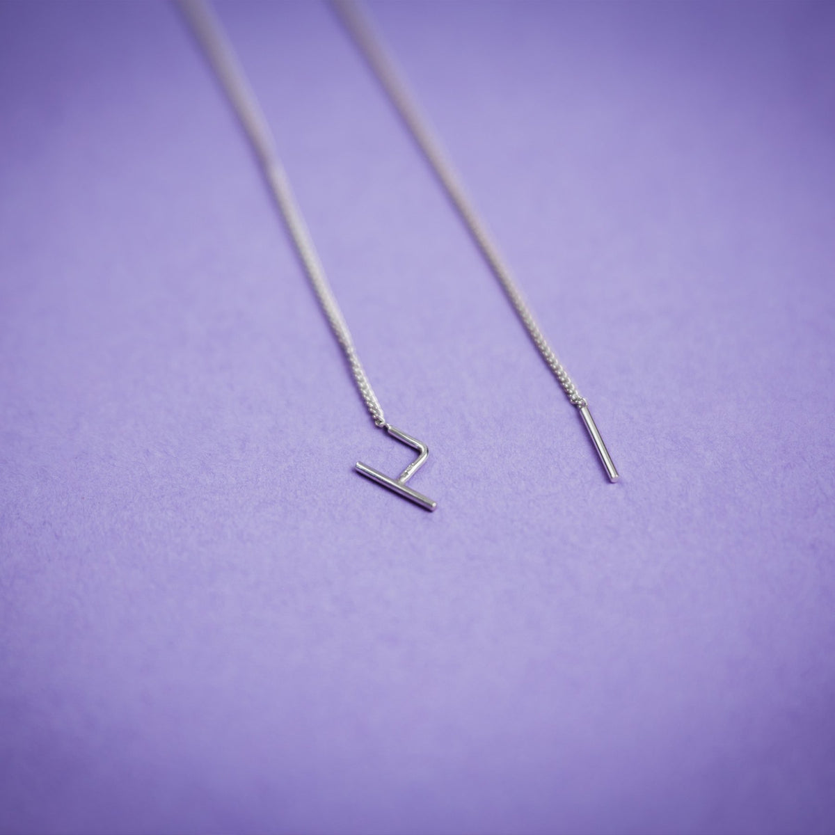 3. Close-up of Maarja Palu SWING earrings with sleek silver chains and bar accents on purple background