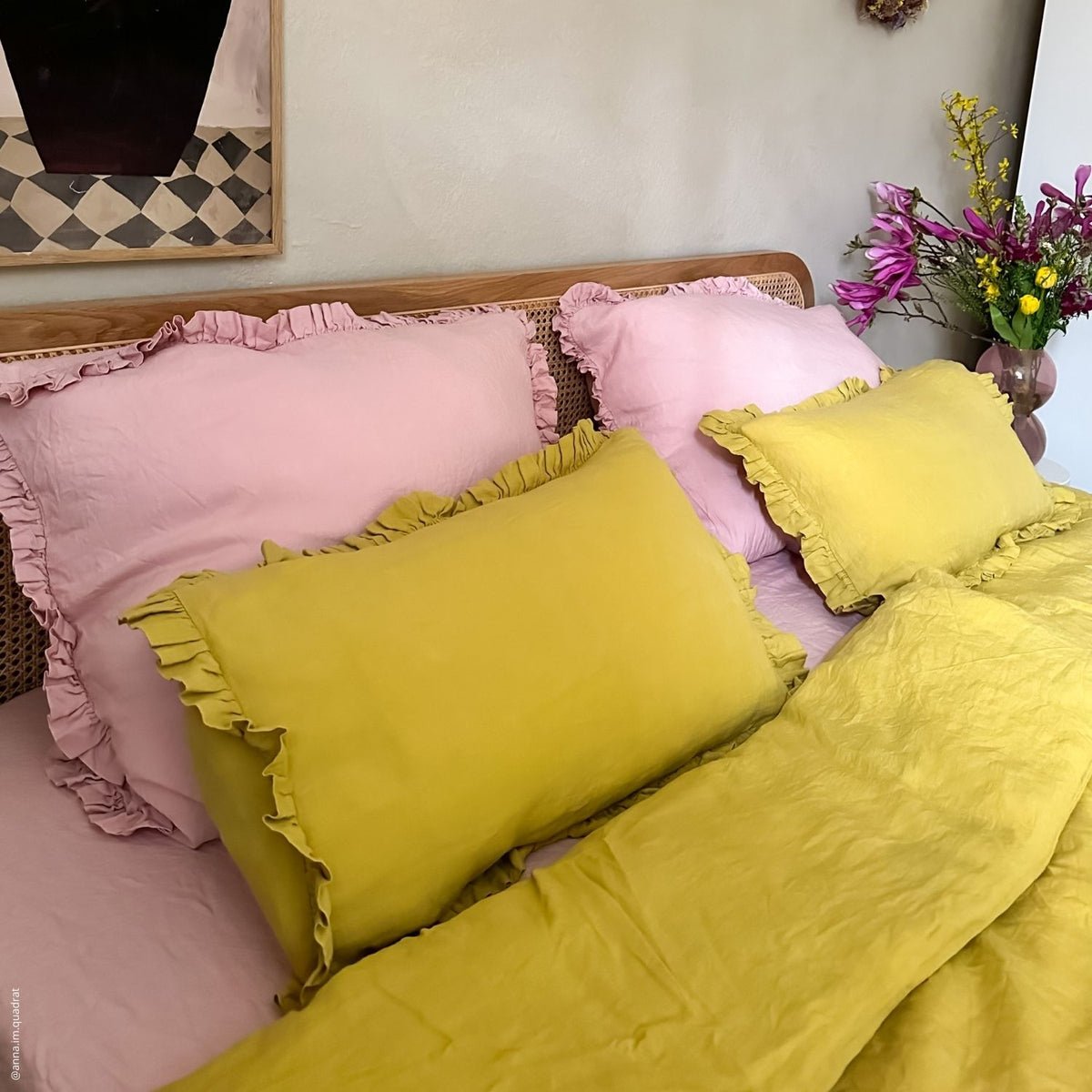 2. Bedroom with pink and yellow frilled linen pillowcases on a bed, complemented by a floral arrangement