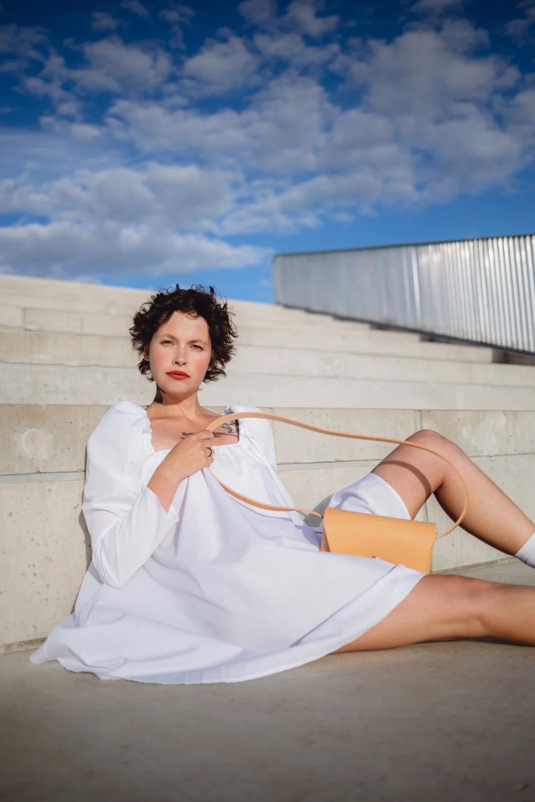 1. Woman in white dress holding Mirgoods beige leather clutch on outdoor steps
