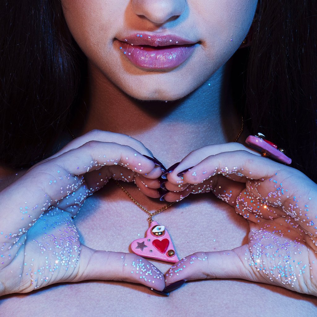 1. Woman holding SCULP All You Need Is Love necklace with ceramic heart pendant and Swarovski crystal, shown in lifestyle setting