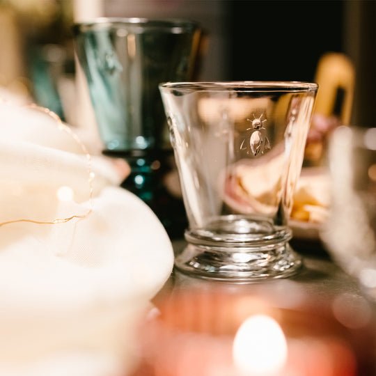 1. Lifestyle shot of La Rochère Bee water glass with embossed bee motif on a table setting with warm lighting
