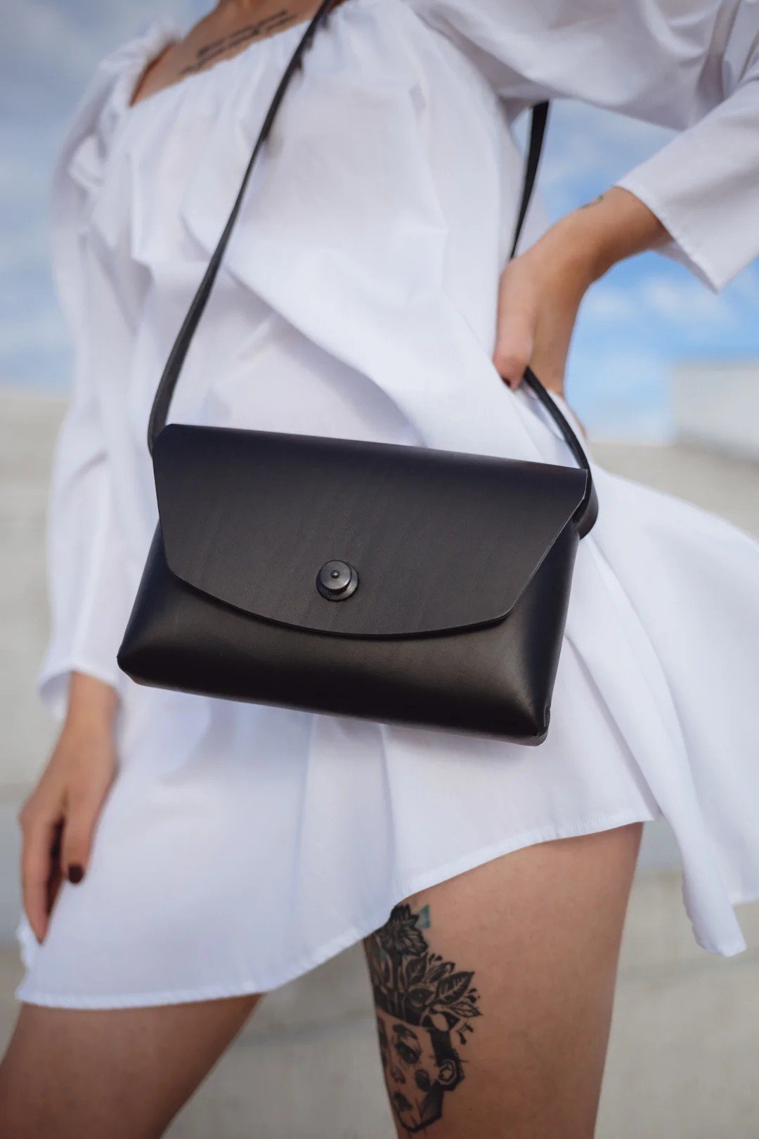 3. Close-up of Mirgoods black leather clutch bag worn with a white dress, highlighting craftsmanship