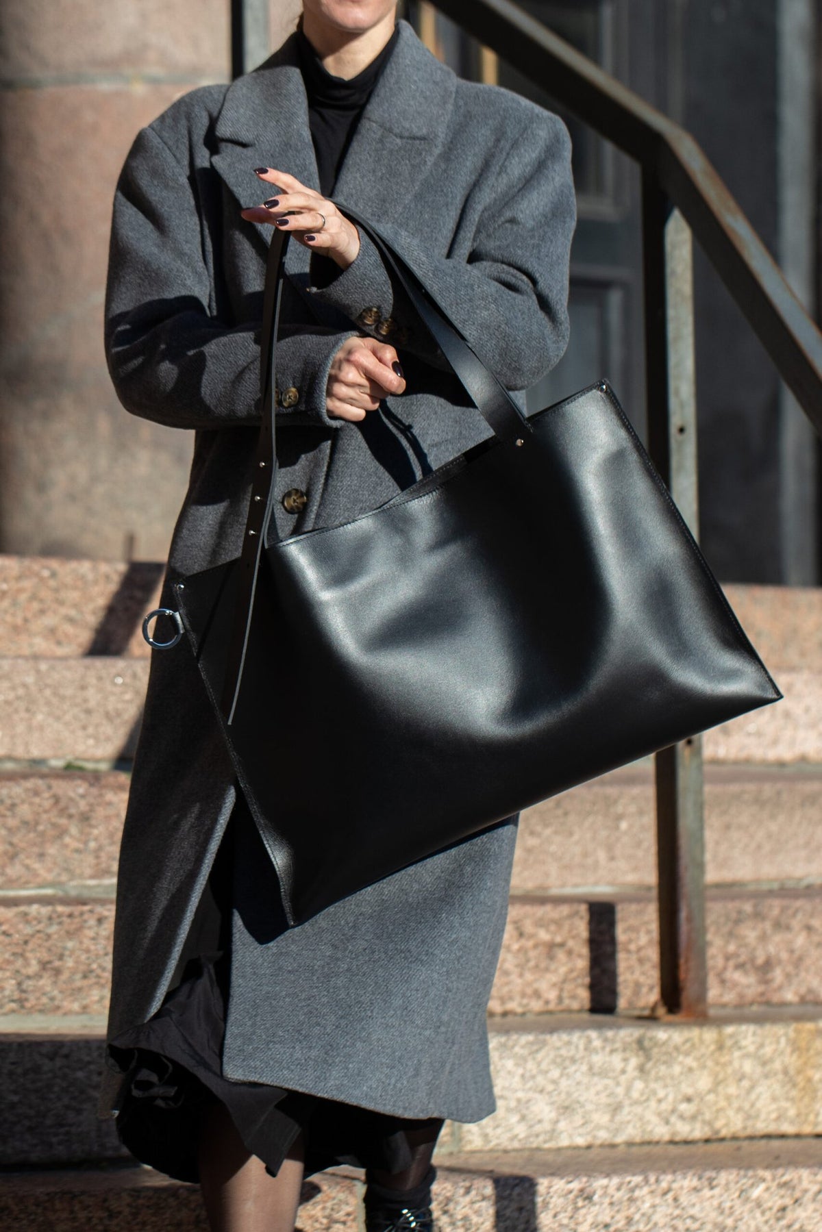 1. Woman carrying PYKOK Adele large handbag in genuine black leather, styled with a grey coat, outdoor setting