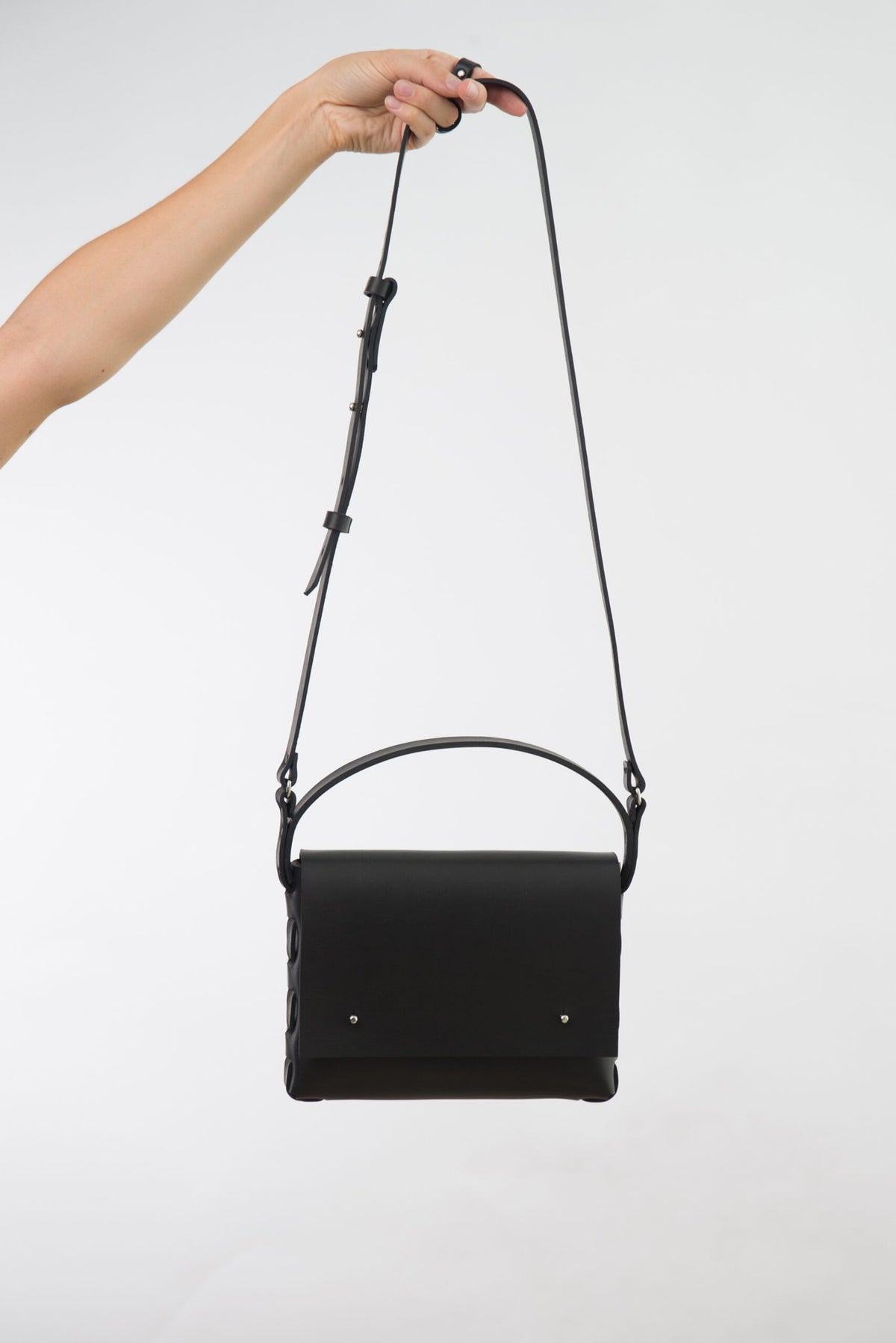 3. Black leather Agatha no.2 handbag by PYKOK, held by hand with adjustable strap visible