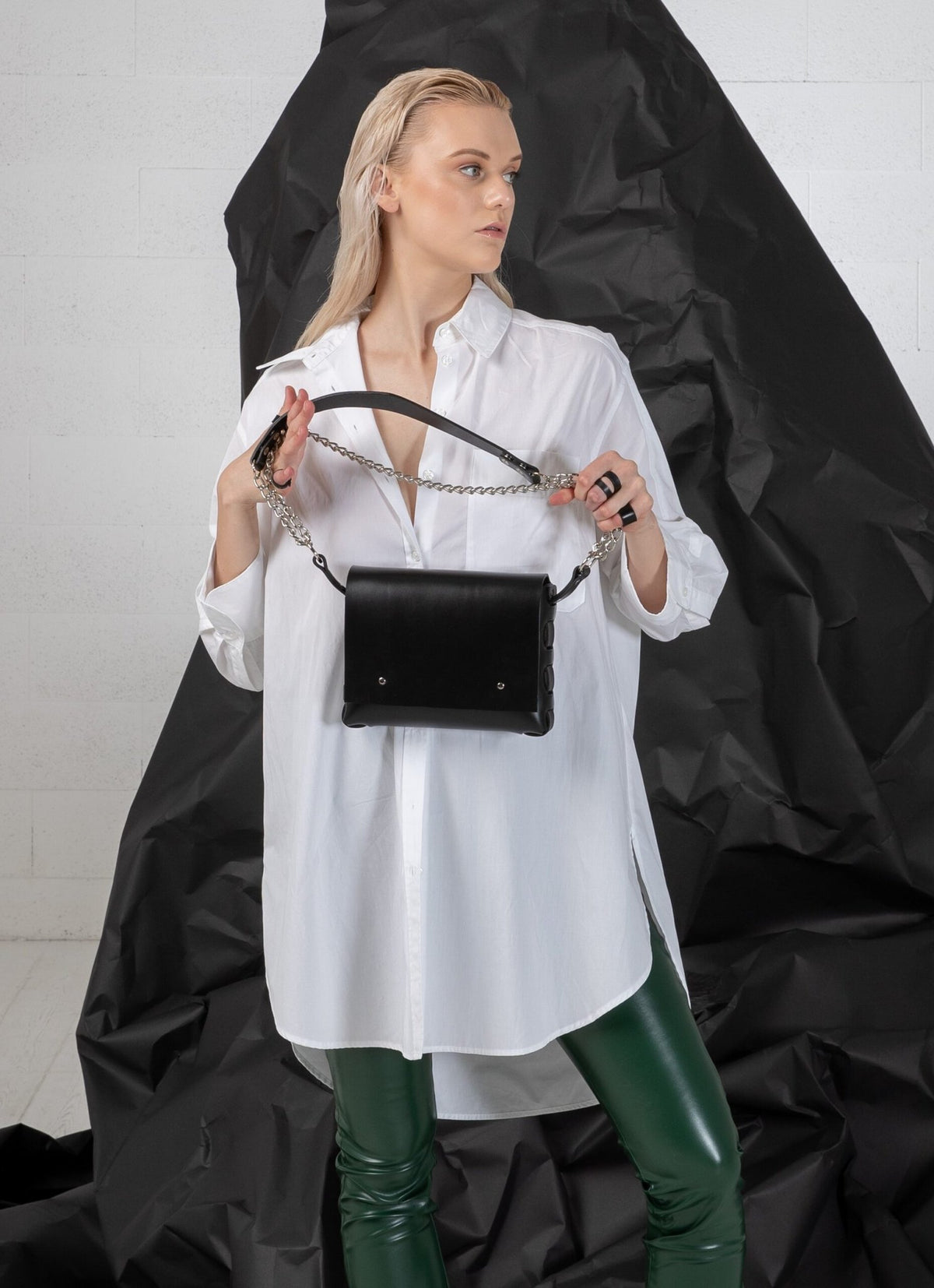 3. Woman holding PYKOK Agatha no.3 handbag with chain and leather strap, styled with white shirt, studio setting