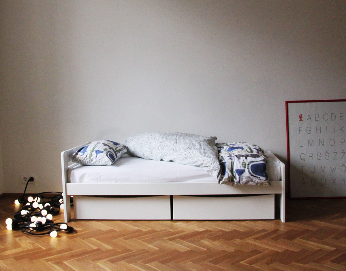 2. White children's bed with patterned bedding and decorative lights on wooden floor