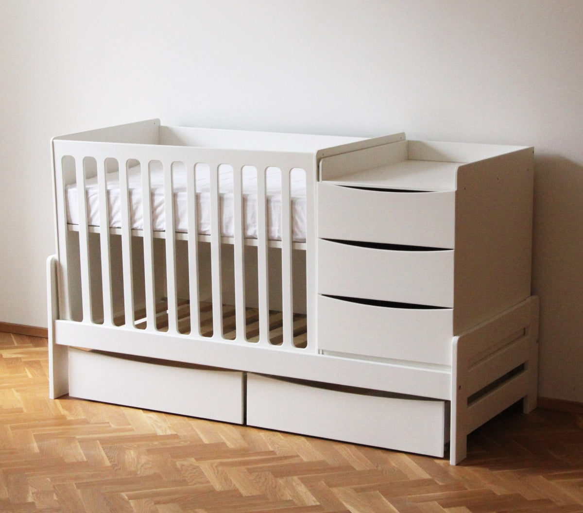 1. White baby crib with attached chest of drawers and changing table on wooden floor