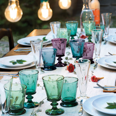 1. Outdoor dining table set with La Rochère Bee Glasses in eggplant, emerald, green, and blue, surrounded by plates and cutlery under warm lighting