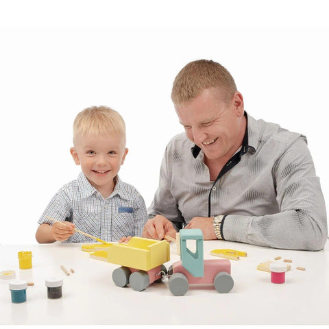 1. Smiling child and adult painting a wooden toy tractor with yellow and pink watercolors, highlighting the interactive DIY aspect
