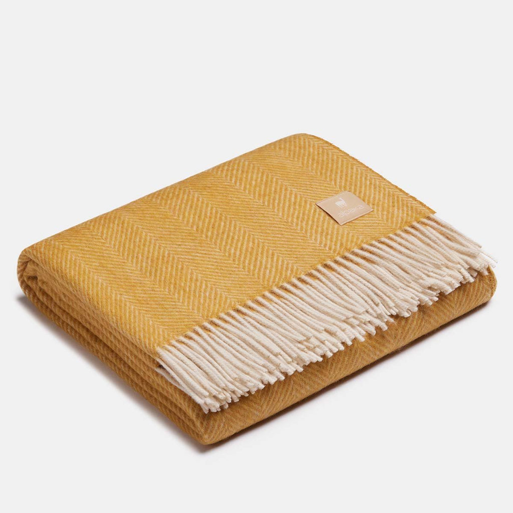 10. Folded mustard yellow Alpaka wool throw with fishbone pattern and fringe in studio