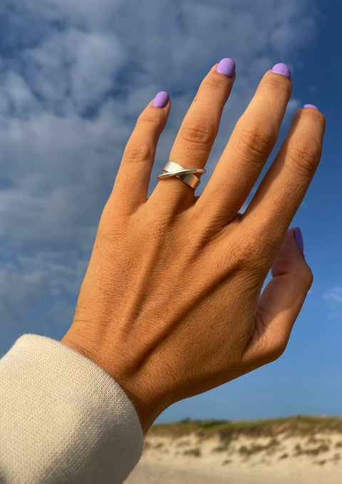 1. Women's hand wearing NO MORE Andromeda Ring in sterling silver, shown outdoors with blue sky background