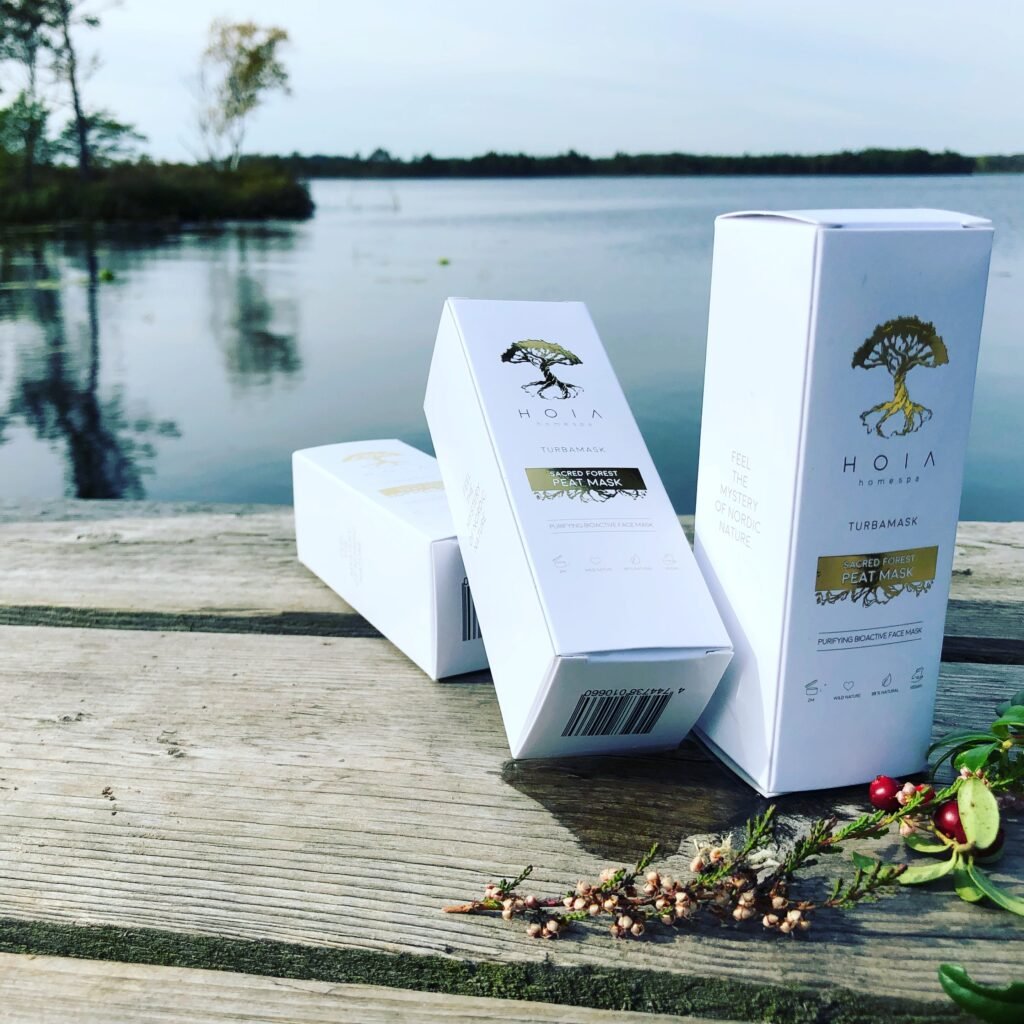 2. HOIA homespa Sacred Forest Peat Mask boxes on wooden deck by a lake, showcasing natural and eco-friendly packaging