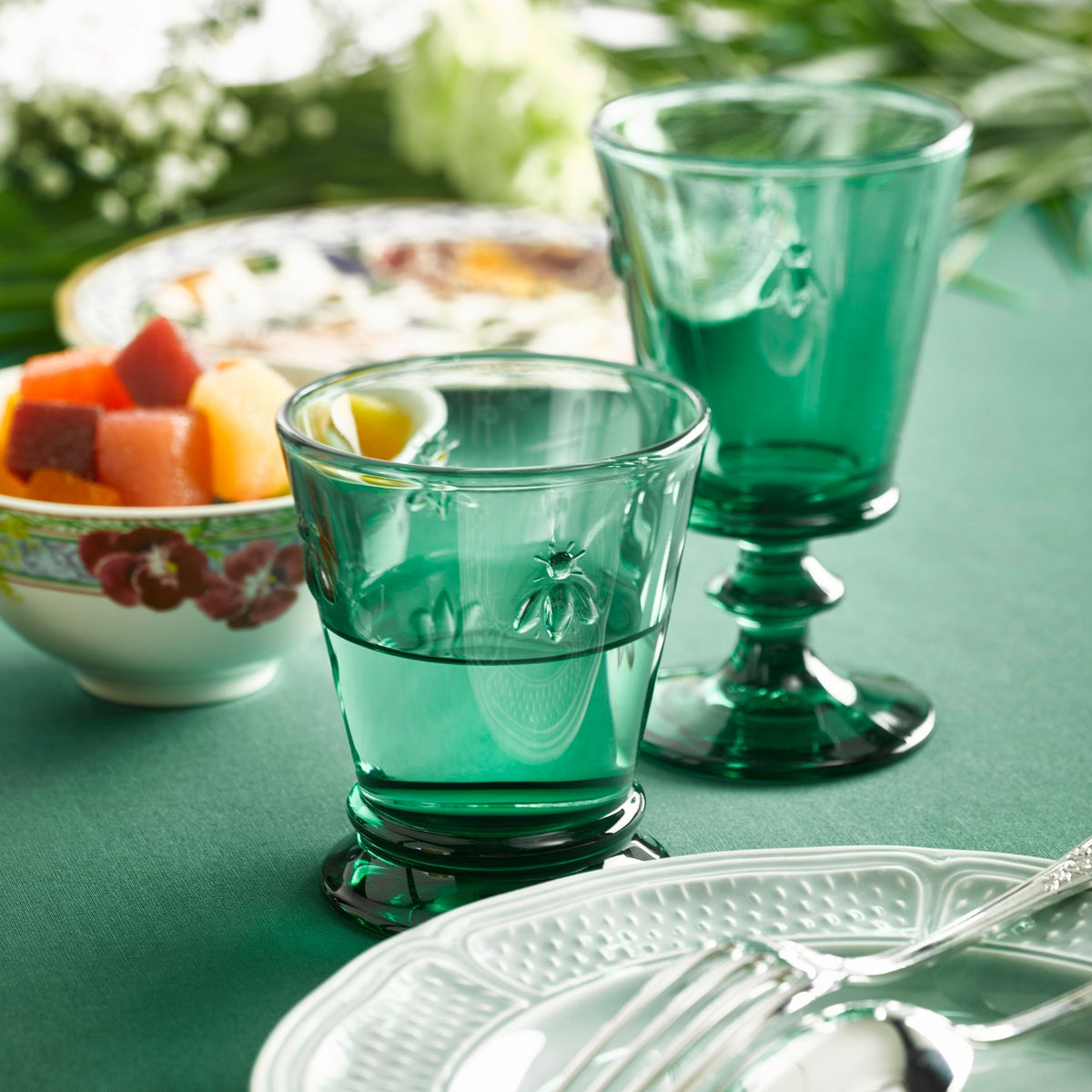 7. Two La Rochère Bee Water Glasses in emerald on a green table setting with fruit bowl and plate