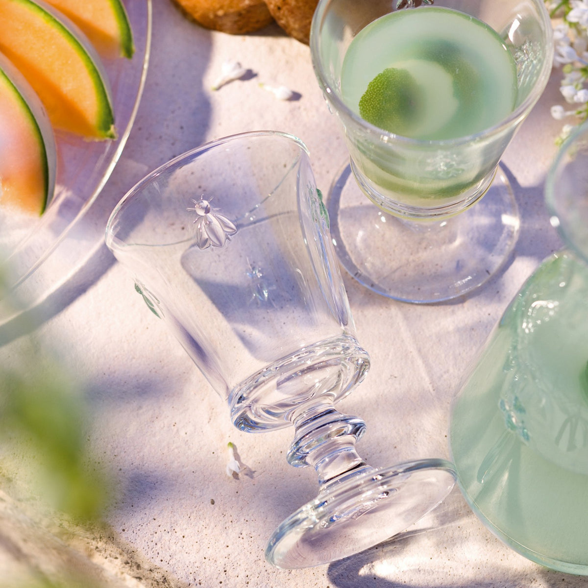 1. Set of La Rochère Bee glasses on a table with drinks and melons, showcasing embossed bee motif