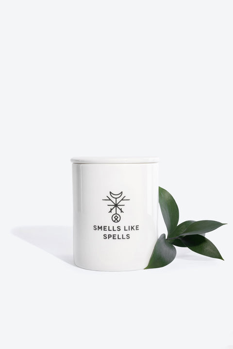 4. Smells Like Spells scented candle in white porcelain container with green leaf accent, studio setting