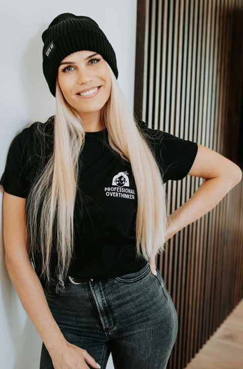 1. Women's black Professional Overthinker T-shirt by Black Giraffe Brand, styled with rolled-up sleeves, worn by model indoors