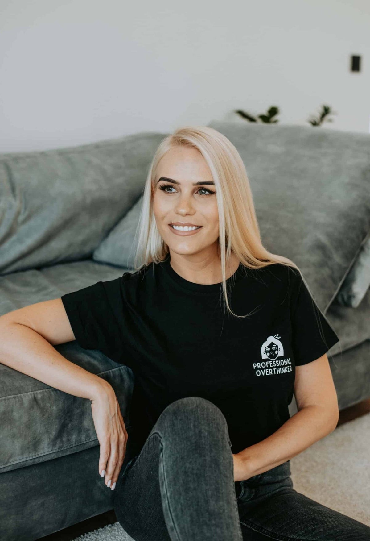 5. Women's black Professional Overthinker T-shirt by Black Giraffe Brand, worn by model sitting on a couch