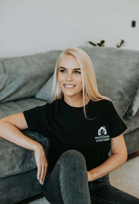 5. Women's black Professional Overthinker T-shirt by Black Giraffe Brand, worn by model sitting on a couch