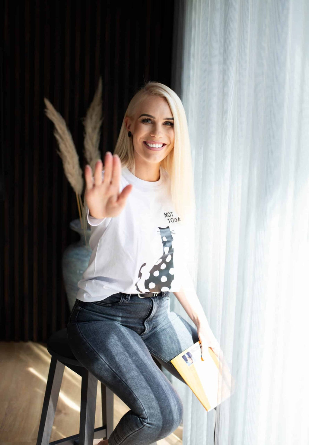 3. Women's white 'Not Today' T-shirt by Black Giraffe Brand, worn by a model sitting on a stool, holding a book